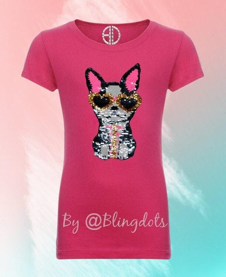 May include: Pink short-sleeved t-shirt with a sequined image of a dog wearing sunglasses. The text "By @Blingdots" is printed on the bottom of the shirt.