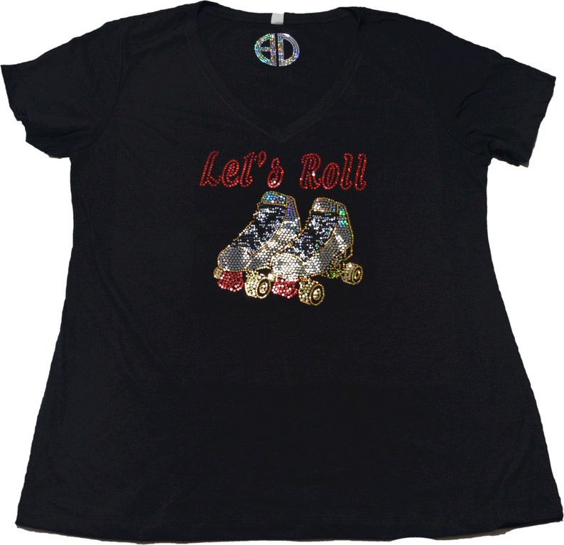 Puede incluir: Camiseta negra con el texto "Let's Roll" en purpurina roja y un par de patines de ruedas en purpurina plateada y dorada.