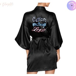 May include: Black satin robe with wide sleeves and a matching belt. The back of the robe features the text "Custom Bling Logo" in a sparkling, multi-coloured design. The robe is a knee-length style.