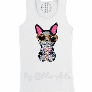 May include: White tank top with a sequined dog wearing sunglasses. The dog is black, white, and gray with pink ears. The text "By @Blingdots" is printed on the bottom of the shirt.