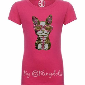May include: Pink short-sleeved t-shirt with a sequined image of a dog wearing sunglasses. The text "By @Blingdots" is printed on the bottom of the shirt.