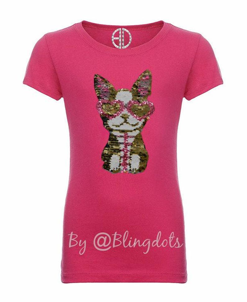 May include: Pink short-sleeved t-shirt with a sequined image of a dog wearing sunglasses. The text "By @Blingdots" is printed on the bottom of the shirt.