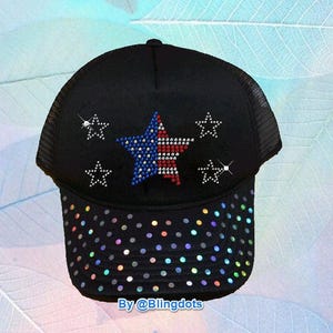 May include: Black trucker hat with a mesh back and a solid front. The front features a large star design in red, white, and blue rhinestones, surrounded by smaller rhinestone stars. The brim is adorned with iridescent rhinestones. The text "By @Blingdots" is at the bottom.