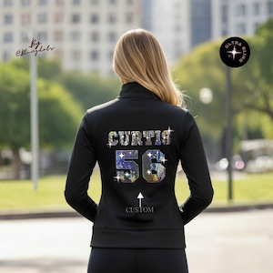 May include: Black zip-up jacket with the name "CURTIS" and the number "56" in a sparkling, colorful design on the back. The word "CUSTOM" is below the number. The jacket is worn by a person.