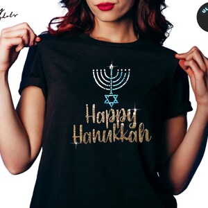 May include: Black t-shirt with a gold glitter design that says "Happy Hanukkah" and a blue and white menorah with a star of David.