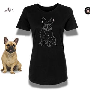 Op de afbeelding: Zwart T-shirt met een witte omtrek van een Franse Bulldog en sprankelende details. Een echte Franse Bulldog staat links van het shirt. De top heeft een ronde hals en korte mouwen. Het T-shirt is effen zwart van kleur.