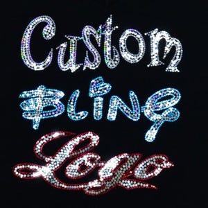May include: A black t-shirt with the words "Custom Bling Logo" in rhinestones. The words are in a stylized font and are arranged in three lines. The rhinestones are silver, blue, and red.