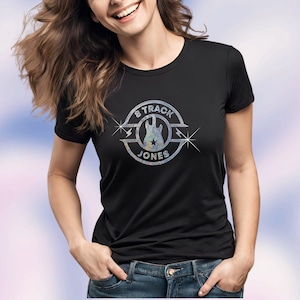 Op de afbeelding: Een zwart T-shirt met een zilveren glitterontwerp van een gitaar en de tekst "8 Track Jones".
