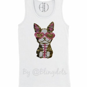 May include: White tank top with a sequined dog wearing pink heart-shaped sunglasses. The dog is brown and gold with pink accents. The text "By @Blingdots" is printed on the bottom of the shirt.