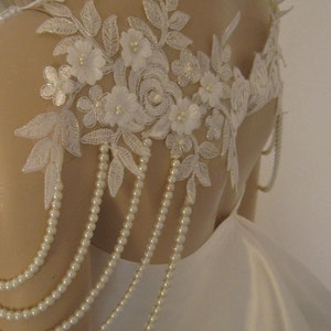 May include: White lace bridal shoulder piece with pearl beading. The lace features delicate floral designs and a pearl trim.