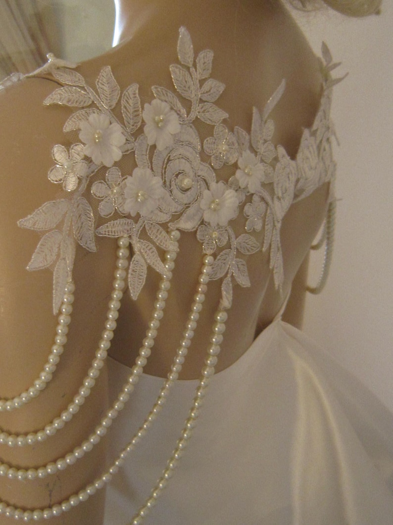 May include: White lace bridal shoulder piece with pearl beading. The lace features delicate floral designs and a pearl trim.