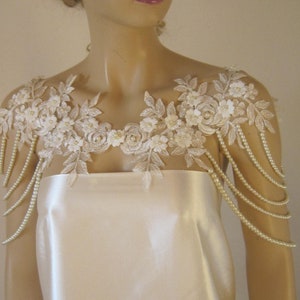 May include: A white lace bridal shoulder piece with pearl beading. The piece is designed to be worn over a strapless dress.
