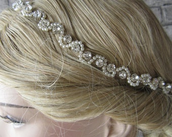 May include: A silver and pearl bridal headband with a delicate design. The headband is made of small, clear rhinestones and pearls, arranged in a flowing pattern. The headband is worn on a model with blonde hair.