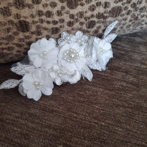 May include: White floral lace applique with pearl embellishments. The applique features three white flowers with pearl centers and delicate lace details.