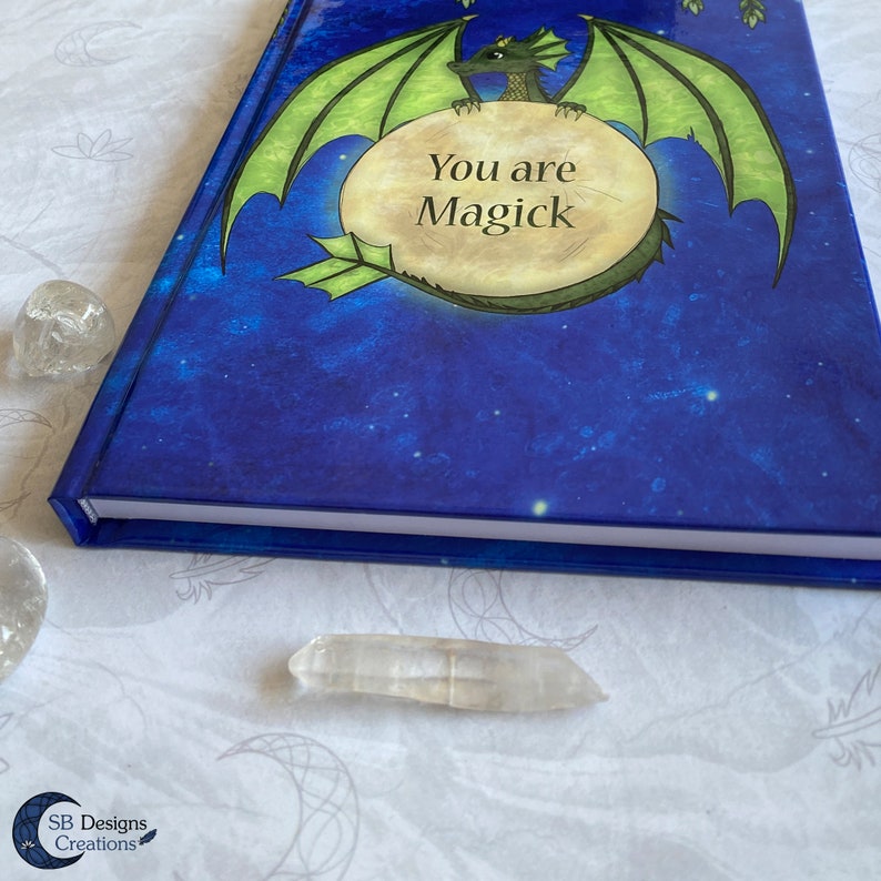 May include: A blue and green journal with a dragon holding a moon-shaped sign that says "You are Magick". The background is a starry night sky.
