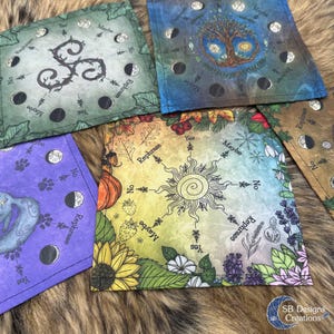 Könnte beinhalten: Eine Sammlung farbenfroher Wahrsage-Tücher mit verschiedenen Designs. Ein Tuch zeigt ein Sonnenstrahl-Design mit botanischen Elementen, während andere Symbole, Monde und Text anzeigen. Die Tücher sind quadratisch und haben ein weiches, strukturiertes Aussehen.