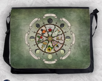 May include: A black messenger bag featuring a green, textured background with a circular wheel of the year design. The graphic includes eight seasonal labels: Yule, Imbolc, Ostara, Beltane, Litha, Lughnasadh, Mabon, and Samhain, alongside moon phases.
