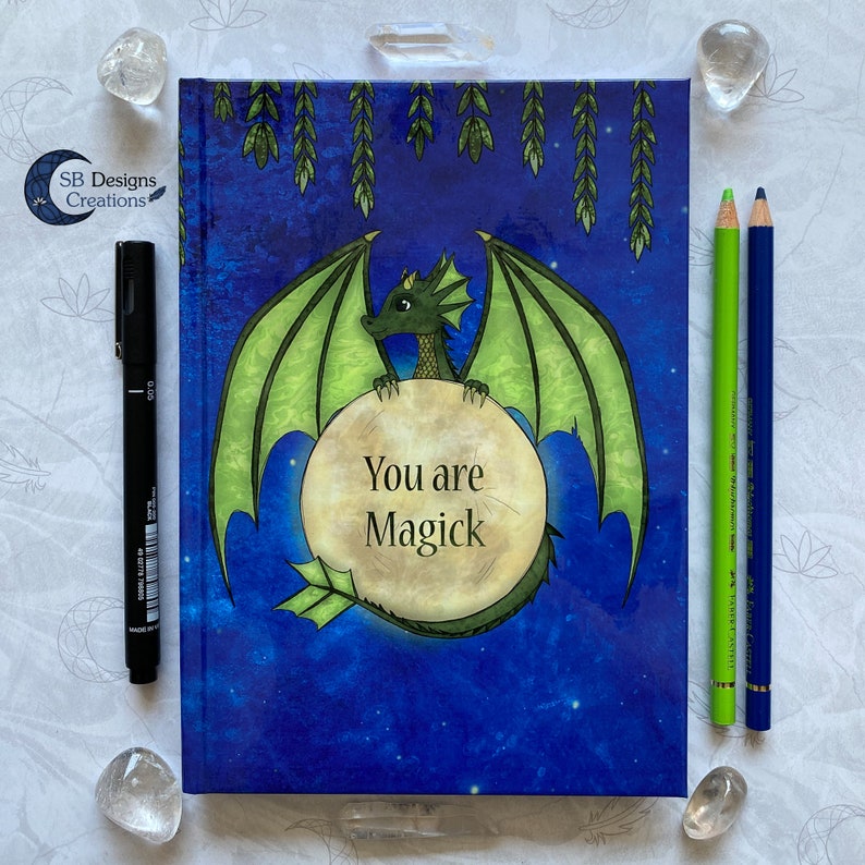 May include: A blue and green journal with a dragon design and the text "You are Magick" on the cover.