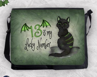 May include: A black messenger bag featuring a green background with a black cat illustration. The cat has green stripes and small fangs. The text reads 13 is my Lucky Number, with the number 13 adorned with small green bat-like wings.