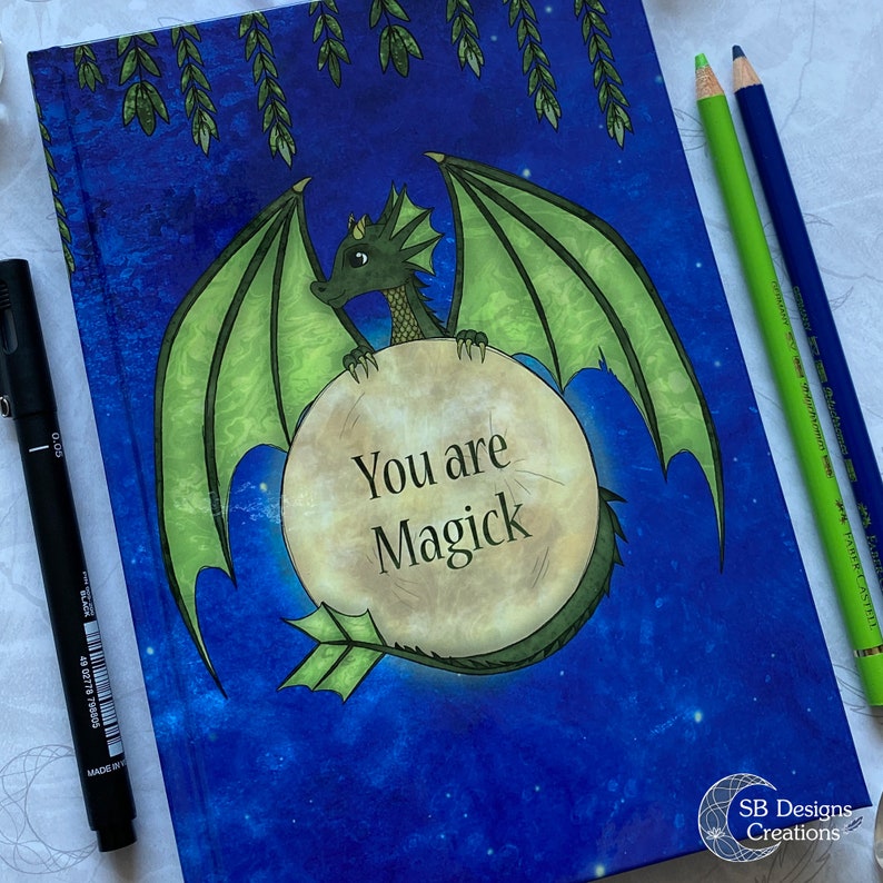 May include: A blue notebook with a green dragon holding a moon with the text "You are Magick" on it. The background is a dark blue with stars and green vines.