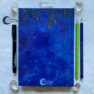 May include: A blue notebook with a starry night sky design and a green leafy border. The notebook has a logo that says "SB Designs Creations" on the front and back covers.