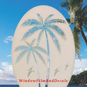 May include: A white oval window cling with a design of two palm trees and three birds. The text "Window Film And Decals" is at the bottom of the cling.