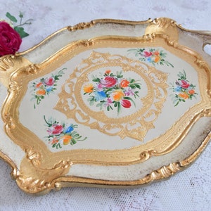 May include: A white and gold serving tray with ornate details and painted floral designs. The tray has two handles and a scalloped edge.