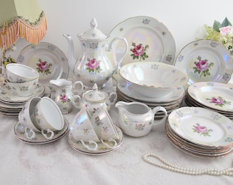 May include: A vintage porcelain tea set with a floral design. The set includes a teapot, creamer, sugar bowl, cups, saucers, and dinner plates. The set is decorated with pink roses and a pearl-like iridescent glaze.