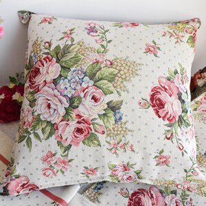 May include: Two decorative throw pillows with a floral pattern featuring pink, red, and white roses on a white background with small white polka dots.