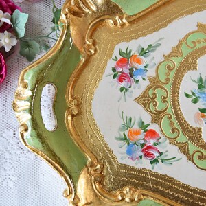 K&ouml;nnte beinhalten: Ein dekoratives Tablett in Gr&uuml;n und Gold mit einer wei&szlig;en Mitte, die mit handgemalten Blumendesigns verziert ist. Das Tablett hat einen gewellten Rand und einen erh&ouml;hten Rand.