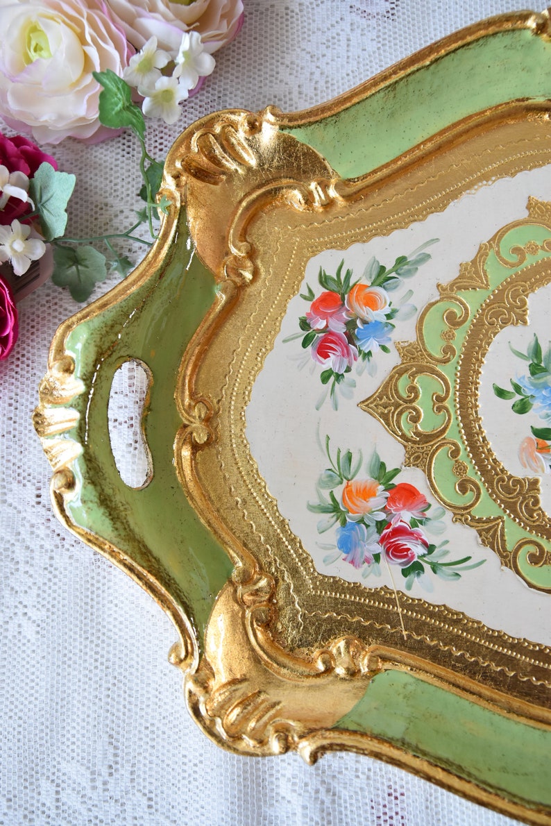 K&ouml;nnte beinhalten: Ein dekoratives Tablett in Gr&uuml;n und Gold mit einer wei&szlig;en Mitte, die mit handgemalten Blumendesigns verziert ist. Das Tablett hat einen gewellten Rand und einen erh&ouml;hten Rand.