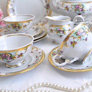 May include: A vintage tea set with floral patterns and gold accents. The set includes a teapot, creamer, sugar bowl, cups, and saucers.
