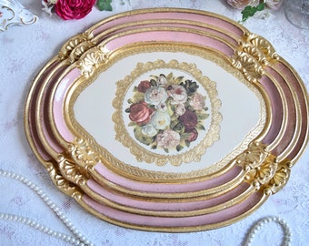 Könnte beinhalten: Ein Set aus drei ovalen Tabletts mit rosa und goldenen, bemalten Rändern. Das größte Tablett zeigt ein Blumenmuster mit einem Rosenstrauß in der Mitte.