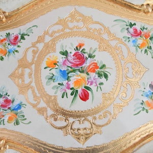 May include: A white oval tray with a gold painted border and floral designs. The center of the tray features a bouquet of pink, red, yellow, orange, and blue flowers.