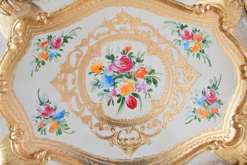May include: A white oval tray with a gold painted border and floral designs. The center of the tray features a bouquet of pink, red, yellow, orange, and blue flowers.
