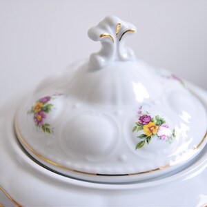 May include: White porcelain teapot with a floral design. The lid has a gold trim and a decorative knob. The teapot has a floral pattern with pink, yellow, and purple flowers.
