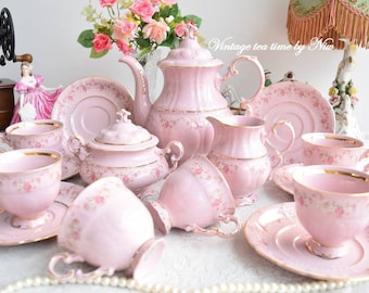 Op de afbeelding: Een vintage roze theeservies met gouden accenten en bloemmotieven. De set bevat een theepot, roomkan, suikerpot en zes theekopjes en schoteltjes.