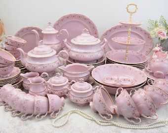 May include: A large pink and gold tea set with floral designs. The set includes teacups, saucers, plates, a teapot, a sugar bowl, a creamer, and a serving dish.