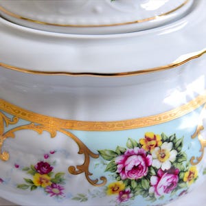 May include: White porcelain teapot with a gold trim and floral design. The teapot has a lid and a handle.