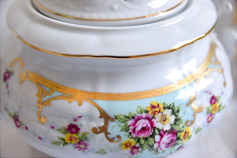 May include: White porcelain teapot with a gold trim and floral design. The teapot has a lid and a handle.