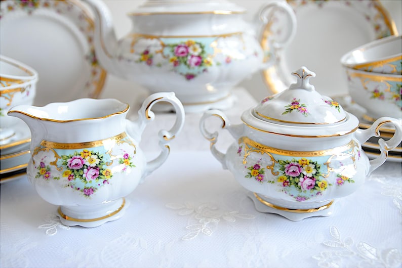 May include: A vintage floral tea set with a teapot, creamer, sugar bowl, and cups. The set is white with gold trim and features a delicate floral pattern in shades of pink, yellow, and blue.