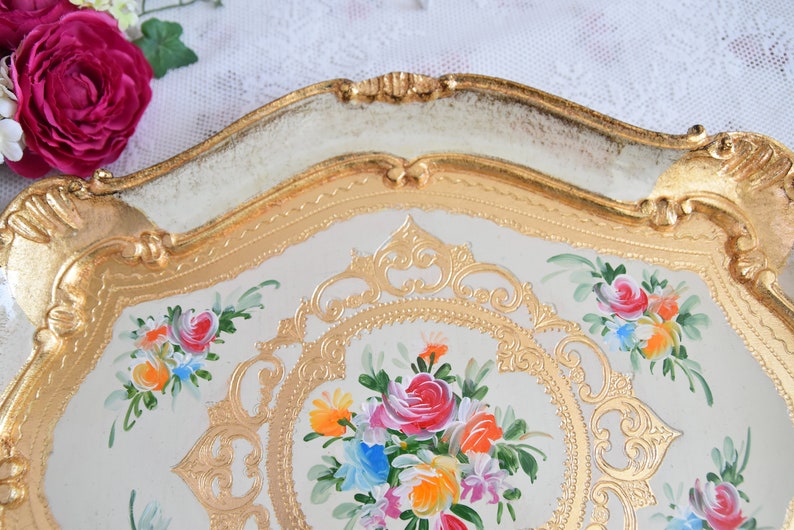 May include: A white and gold decorative tray with a floral design. The tray has a raised rim with gold accents and a floral pattern painted on the surface.