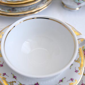 May include: A white teacup with a gold rim and a floral pattern on the saucer. The teacup is empty and the saucer has a light blue background.
