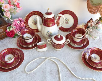 May include: A red and gold tea set with a teapot, sugar bowl, creamer, and four teacups and saucers. The set is decorated with floral designs and gold trim.