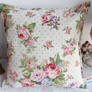May include: A beige pillow with a white polka dot pattern and a floral design featuring pink, red, and green roses.
