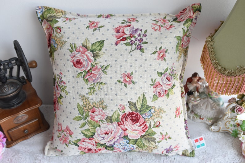 May include: A beige pillow with a white polka dot pattern and a floral design featuring pink, red, and green roses.