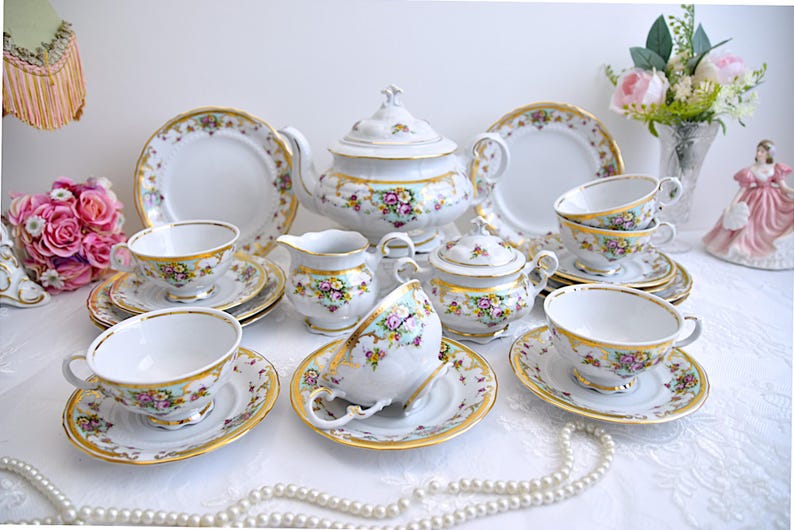 May include: A vintage porcelain tea set with floral and gold accents. The set includes a teapot, creamer, sugar bowl, and four teacups and saucers.