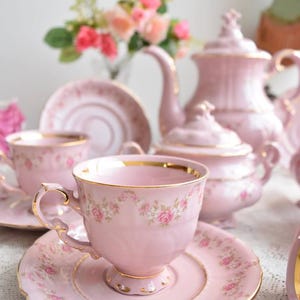 Puede incluir: Un juego de t&eacute; rosa con ribetes dorados y dise&ntilde;os florales. El juego incluye una tetera, una jarra de crema, un azucarero y dos tazas de t&eacute; y platillos.
