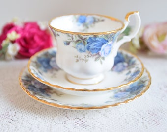 May include: A white teacup and saucer set with a blue rose pattern and gold trim. The set is made of fine china and is perfect for afternoon tea.