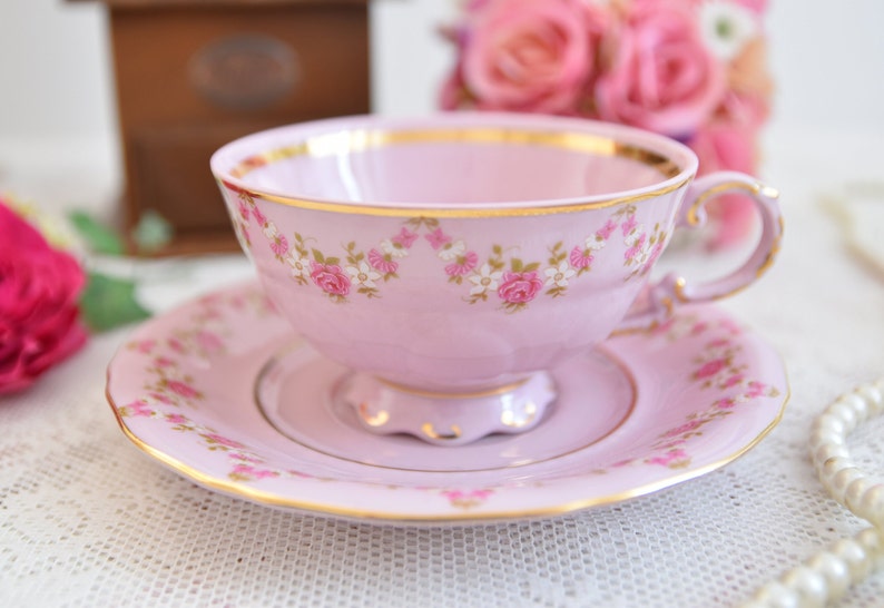 Elegant tea cup and saucer with rose garland and gold trim on lace tablecloth.